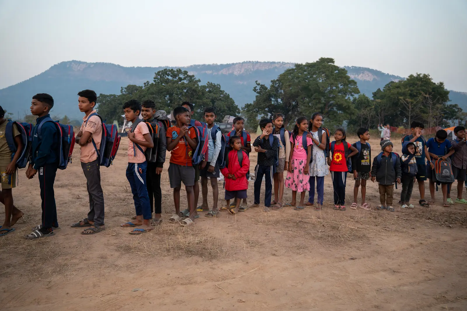 A line of schoolchildren with their new backpacks against a mountain backdrop