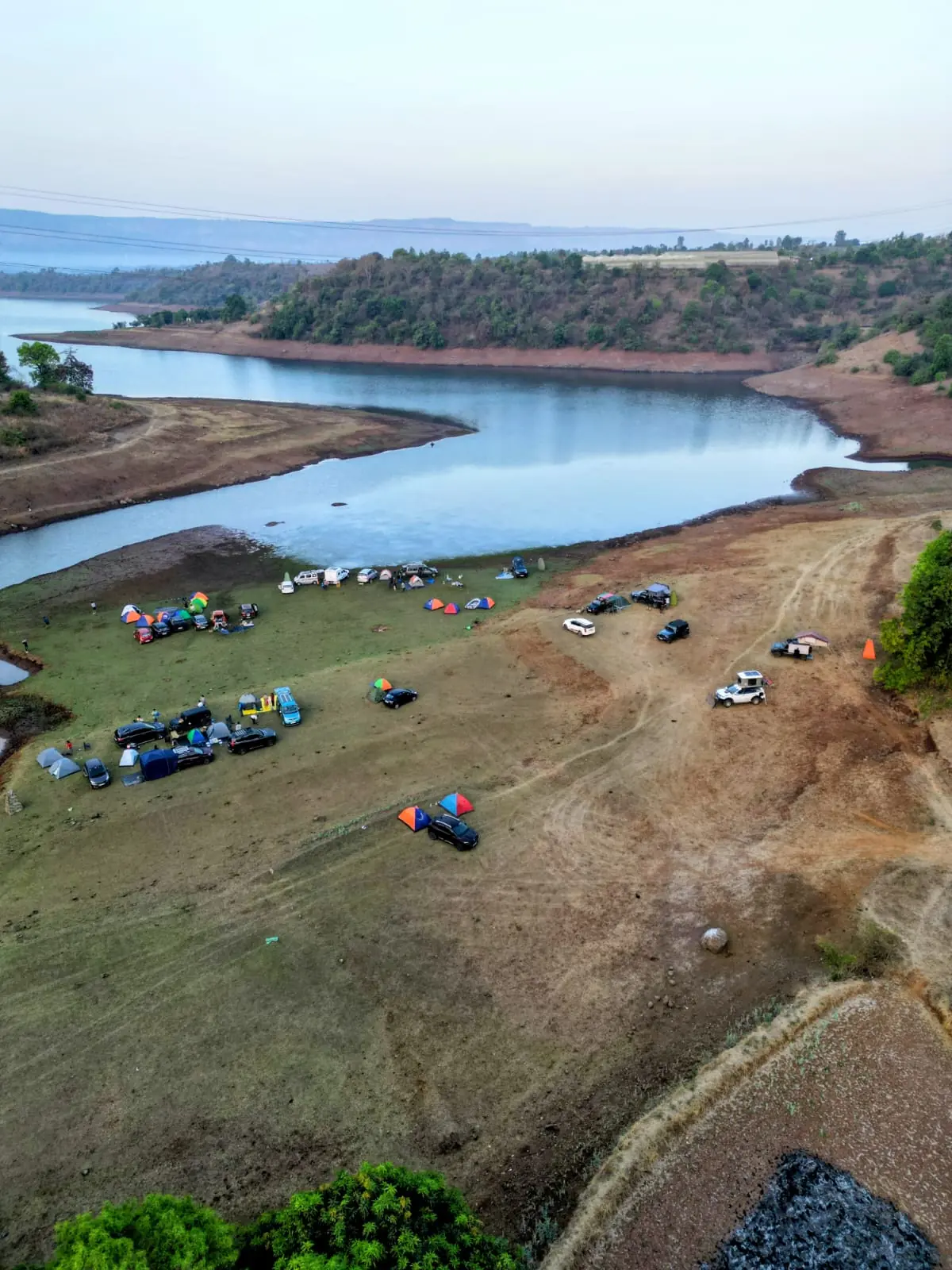 Aerial view of an overlander campsite beside a lake with colourful tents and vehicles