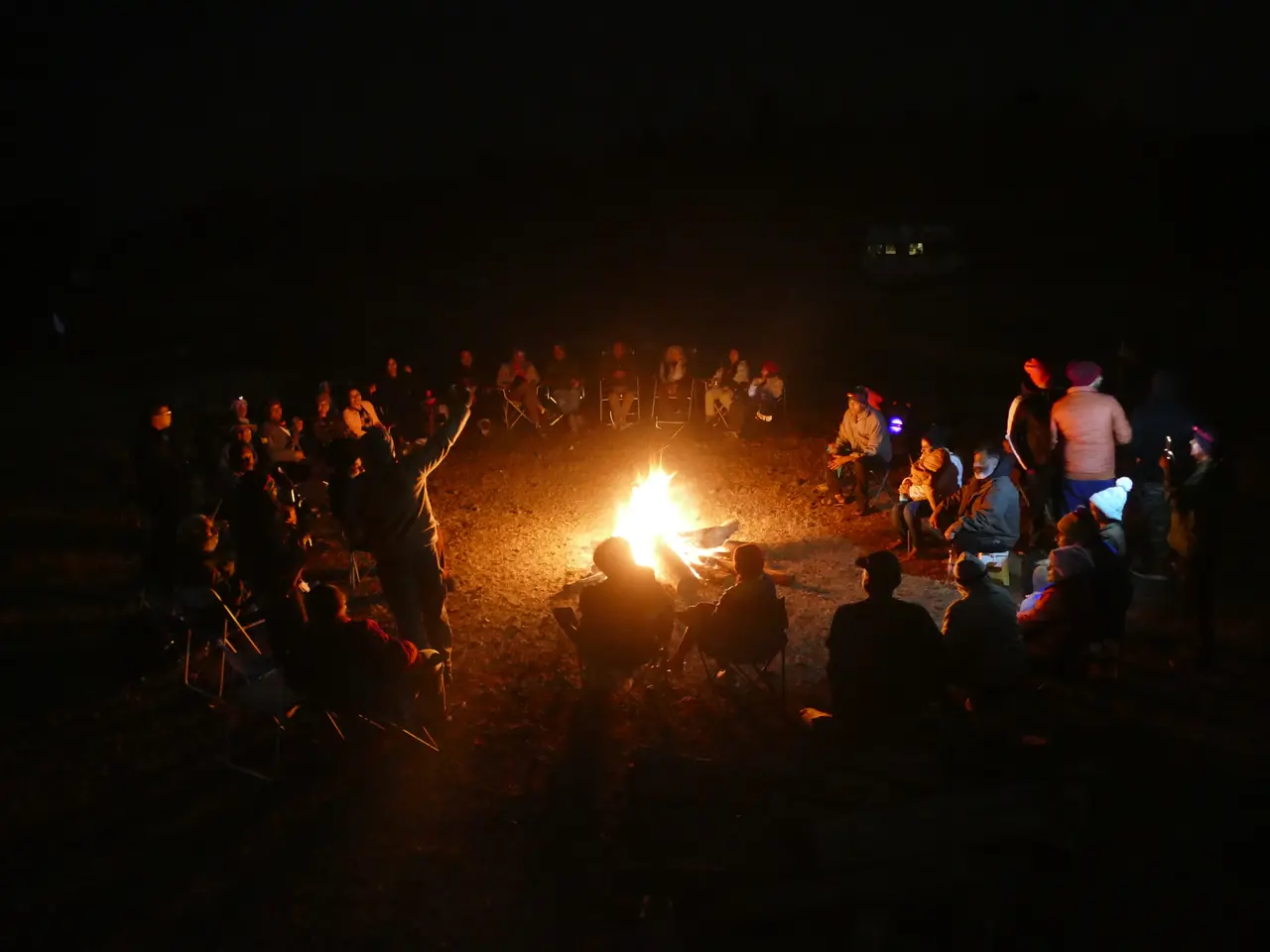 Members gathered in a circle around the campfire at night
