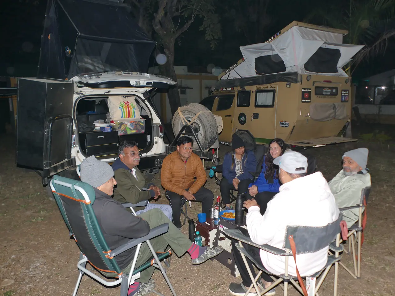 Members chatting around camp chairs beside their overlanding rigs at night