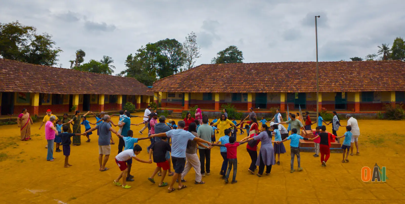 OAI members and local schoolchildren dancing in a circle at a Coorg village school