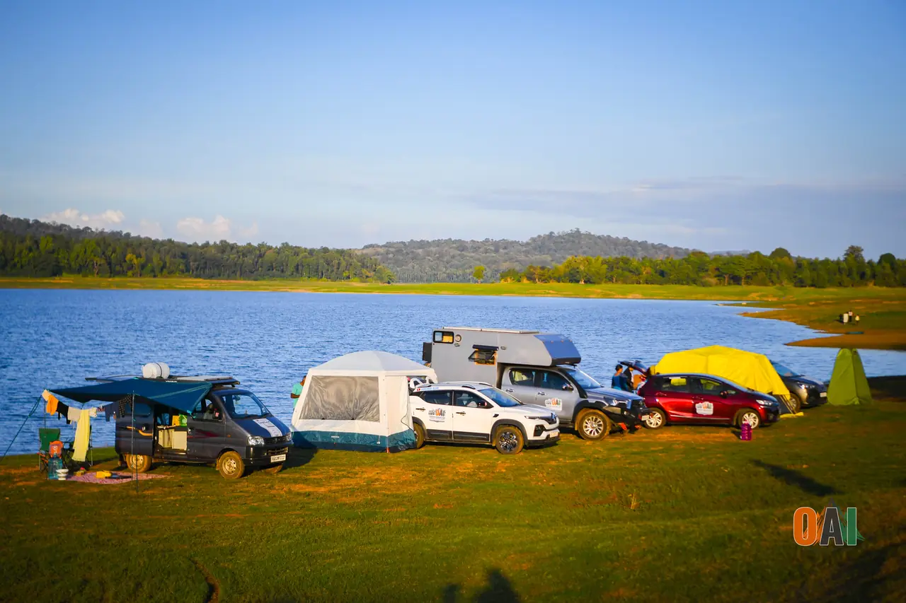 Overlander vehicles and tents camped beside the Harangi backwaters at golden hour